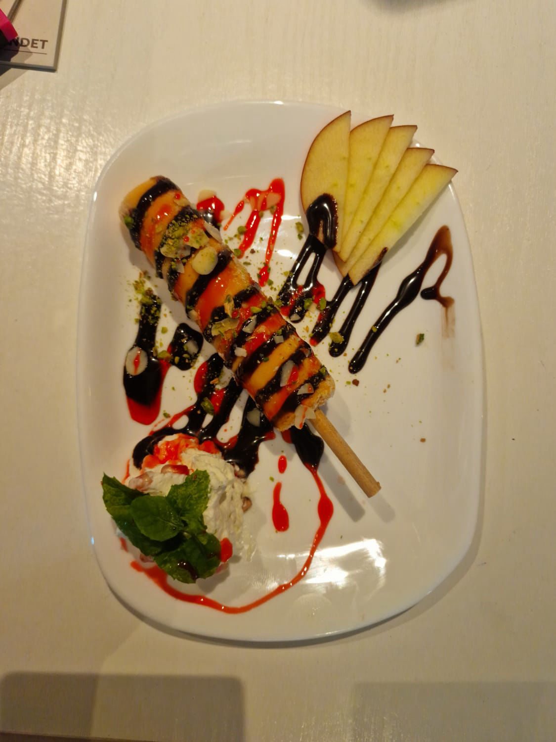 Kulfi am Stiel mit Apfelscheiben und Soßendekor auf weißem Teller