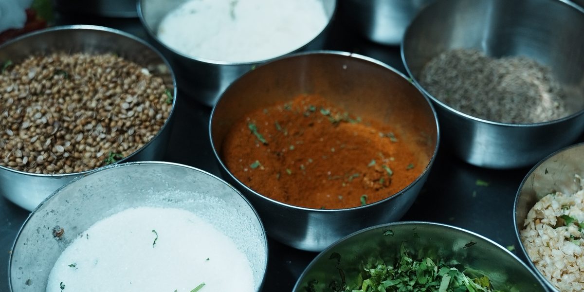 Metallschalen mit Gewürzen, Joghurt, frischem Koriander und Soßen in der Küche