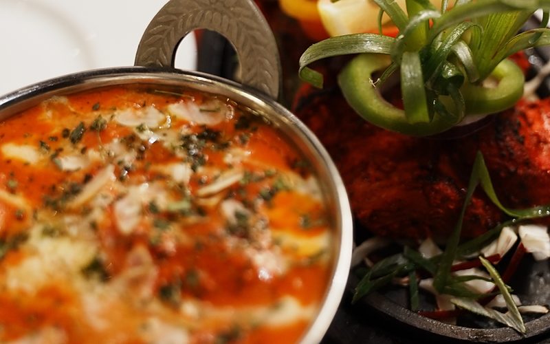 Cremiges Hähnchen-Curry im Karahi neben Tandoori-Hähnchen mit frischer Garnitur