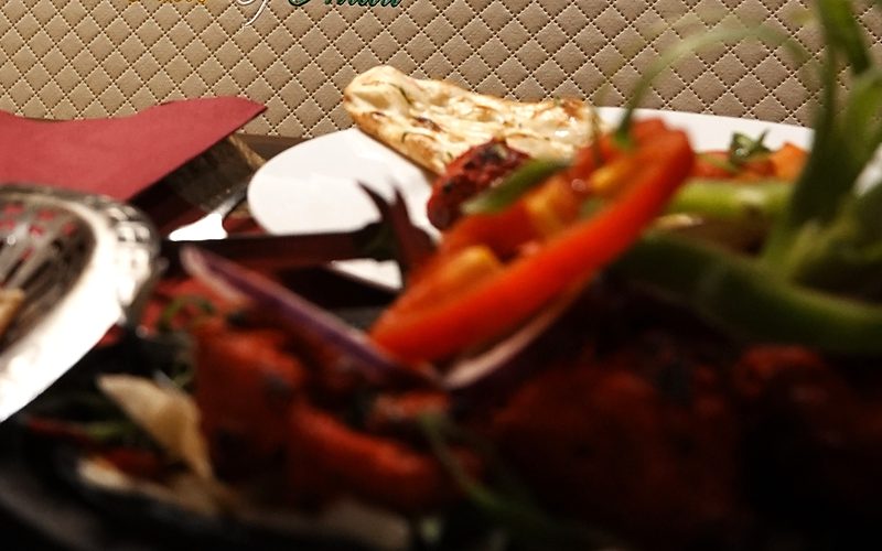 Tandoori-Hähnchen mit Paprika und Zwiebeln auf der heißen Platte, dahinter Naan-Brot