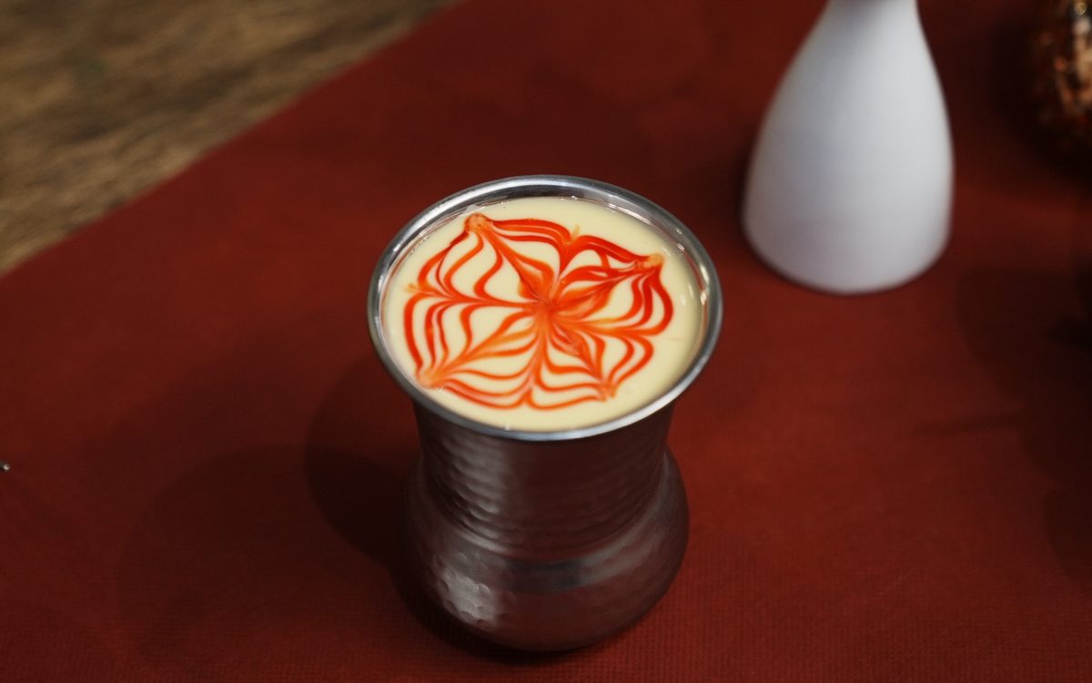 Mango Lassi im gehämmerten Metallbecher, oben mit rotem Soßenmuster verziert