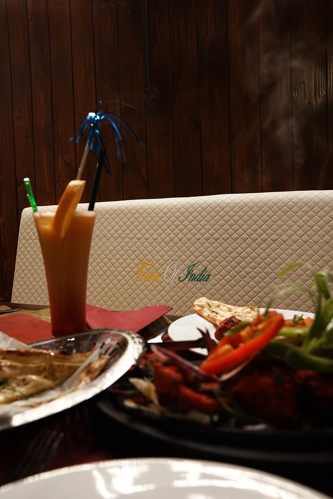 Tandoori-Platte mit Paprika und Naan-Brot, daneben ein fruchtiges Getränk vor der bestickten Sitzbank