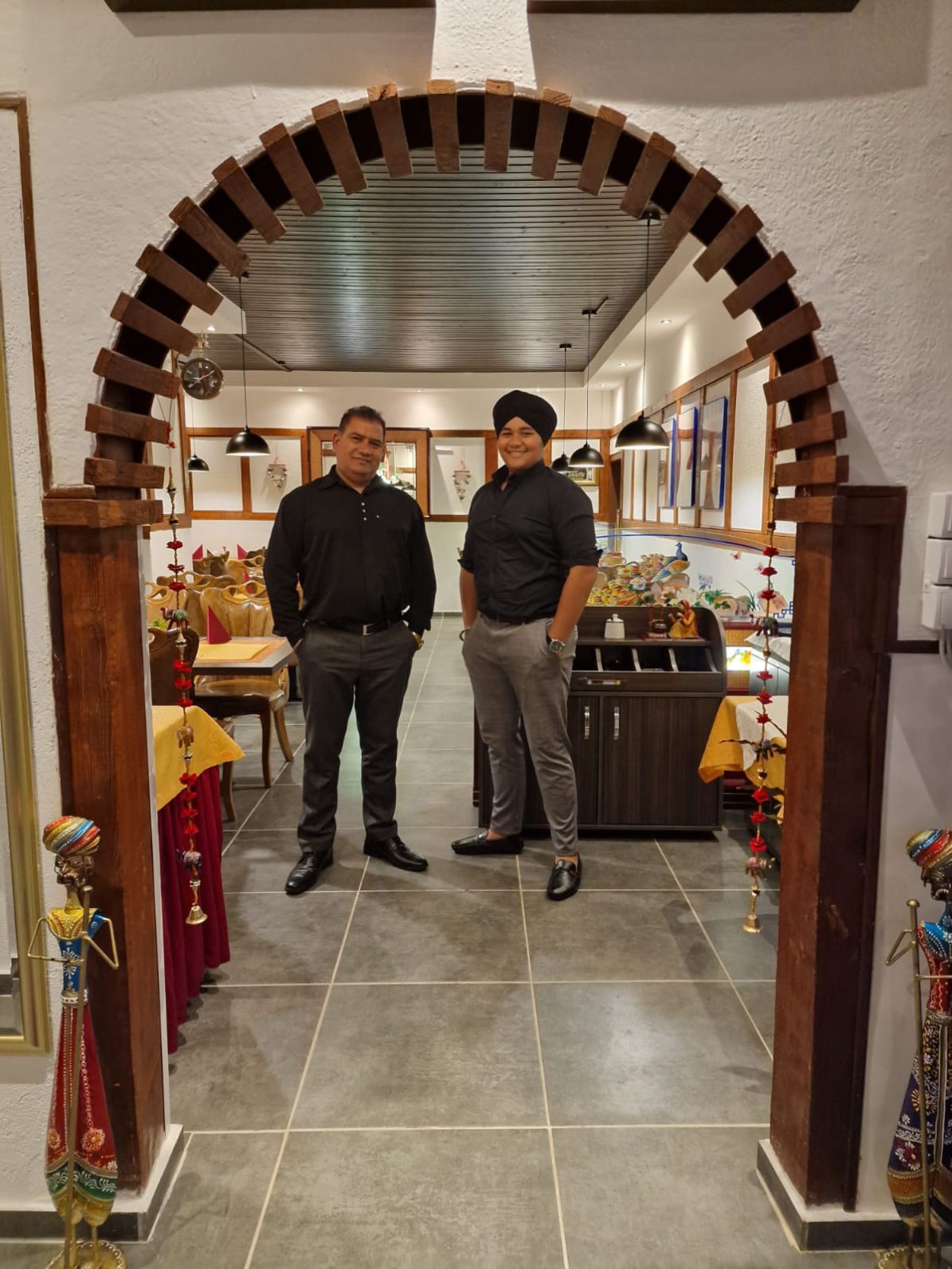 Zwei Gastgeber von Taste of India stehen im holzverkleideten Eingangsbogen des Restaurants
