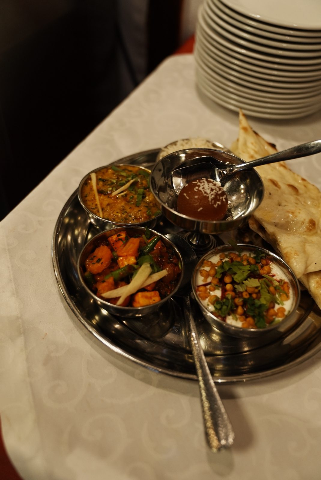 Thali-Platte mit Schälchen voll Curry, Kichererbsen und Gemüse, dazu Naan-Brot