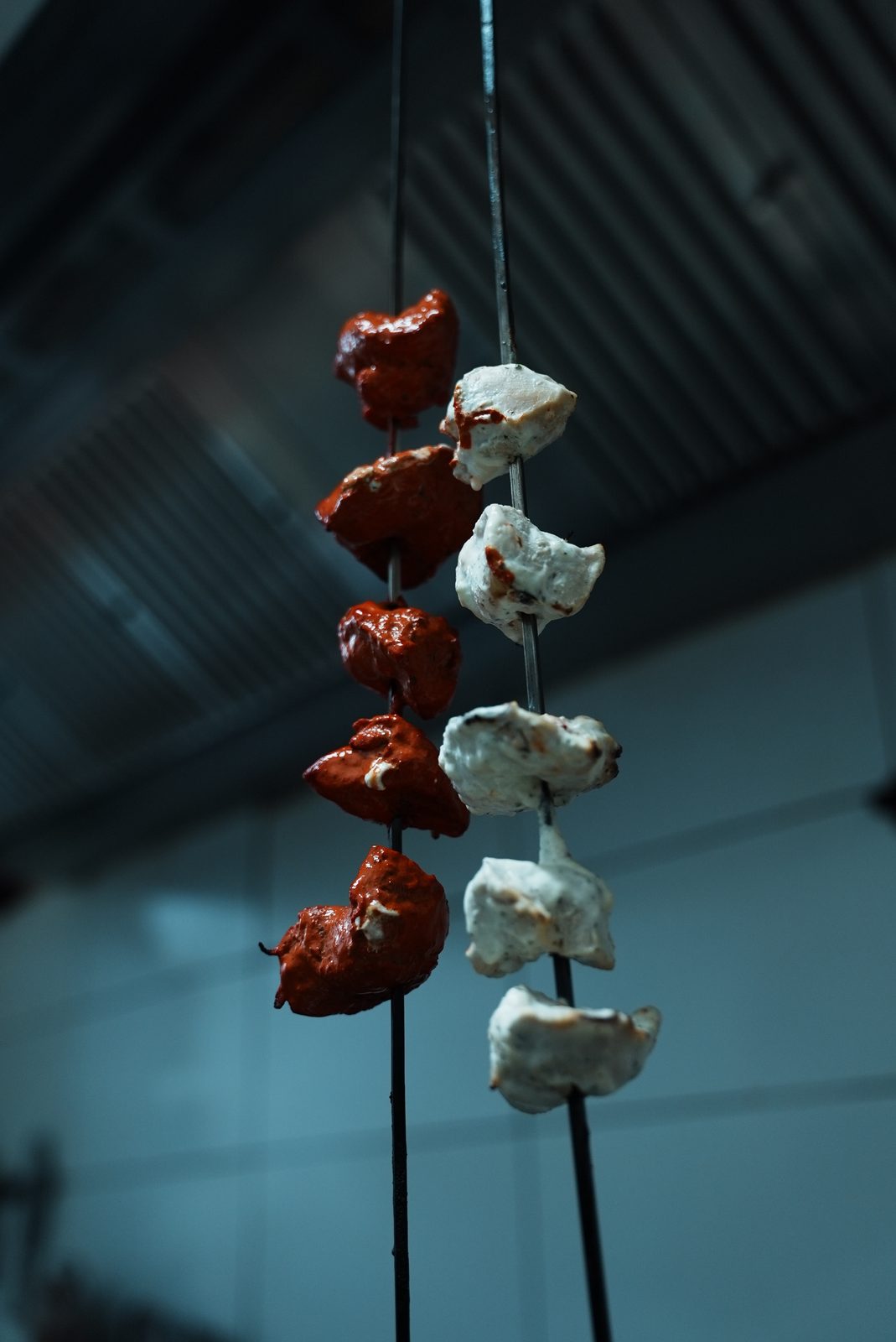 Rot und hell marinierte Hähnchenstücke auf langen Tandoor-Spießen in der Küche