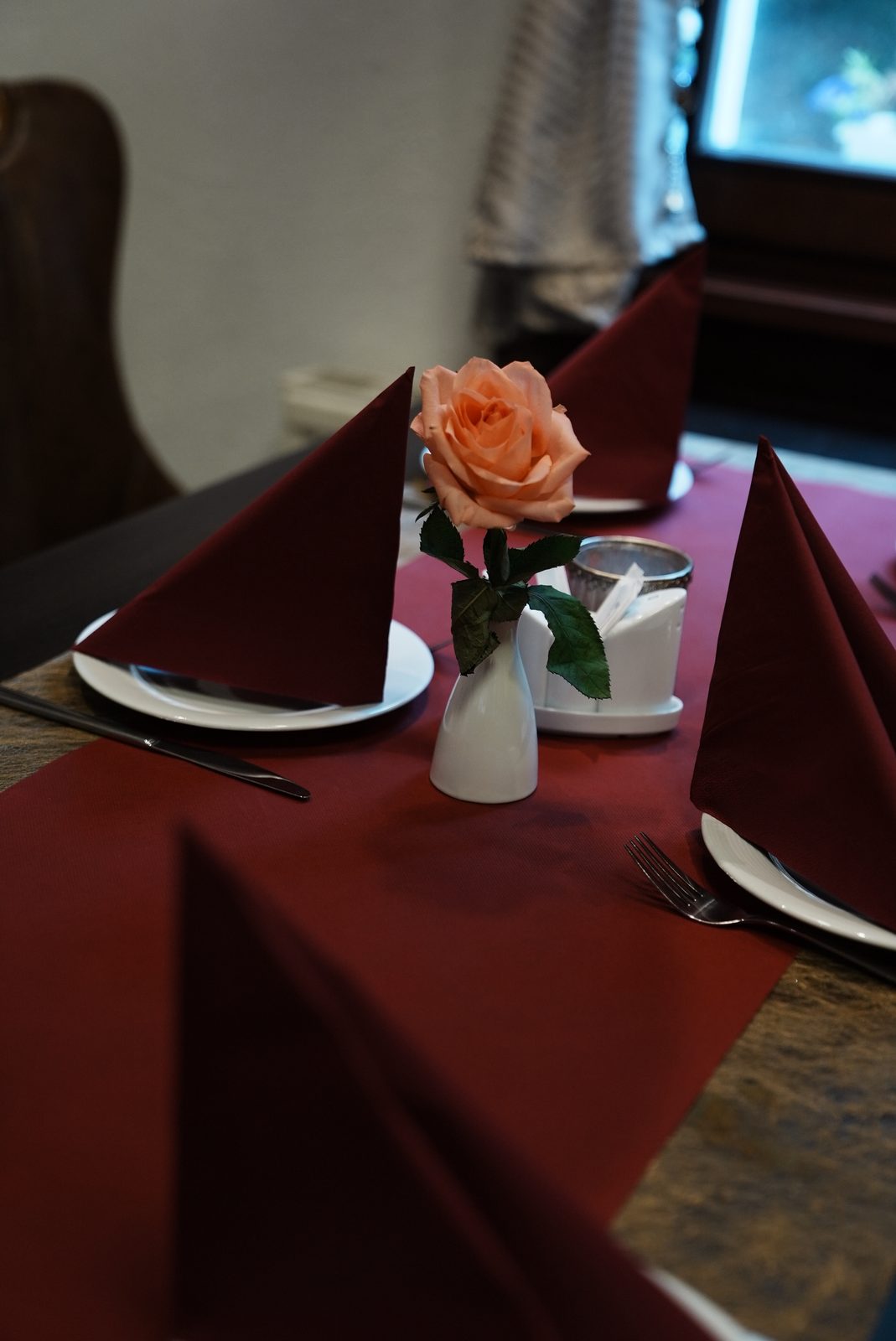 Eingedeckter Tisch mit roten Servietten und einer Rose in der Vase